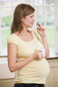 Pregnant woman standing in kitchen with coffee and cigarette